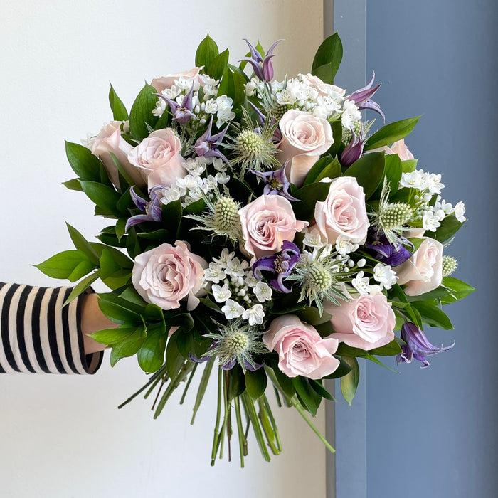 Our lovely Hope Pink roses mixed with a touch of dainty white alliums, purple clematis, silvery-green eryngiums, and single ruscus, makes this lovely Sofia bouquet.